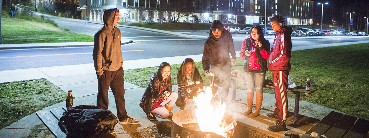 51 students roast marshmallows around a fire pit on campus